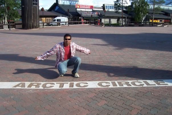 Gagan crouching beside an Arctic Circle marker