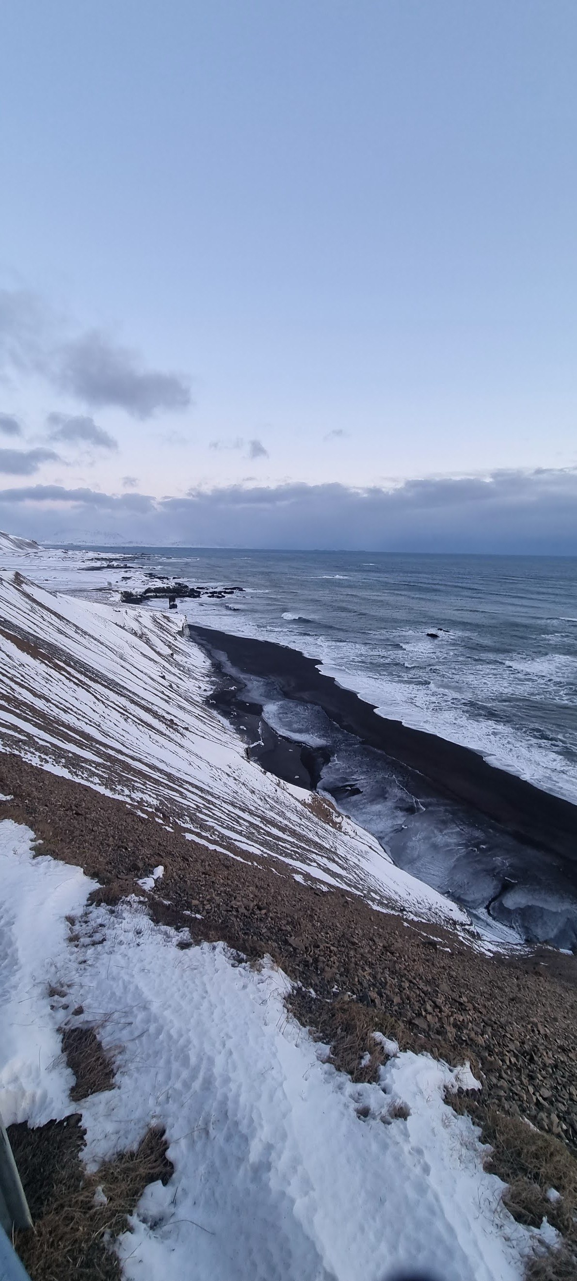 Snow above a dark shoreline and the sea