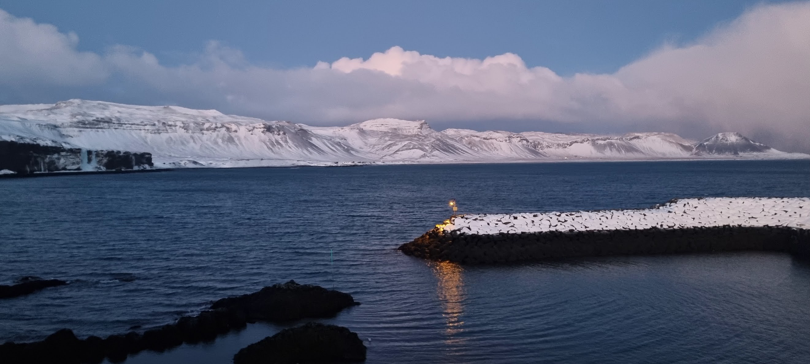 Water, a stone breakwater and snow-covered mountains