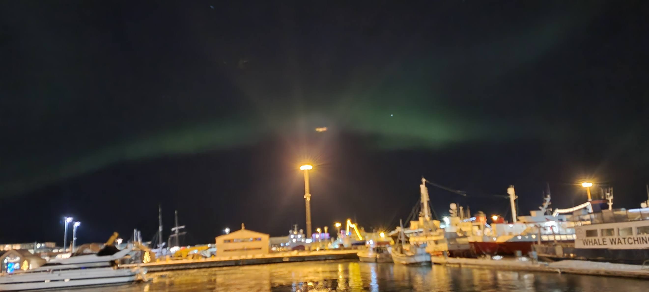 A faint green glow in the night sky above a harbor