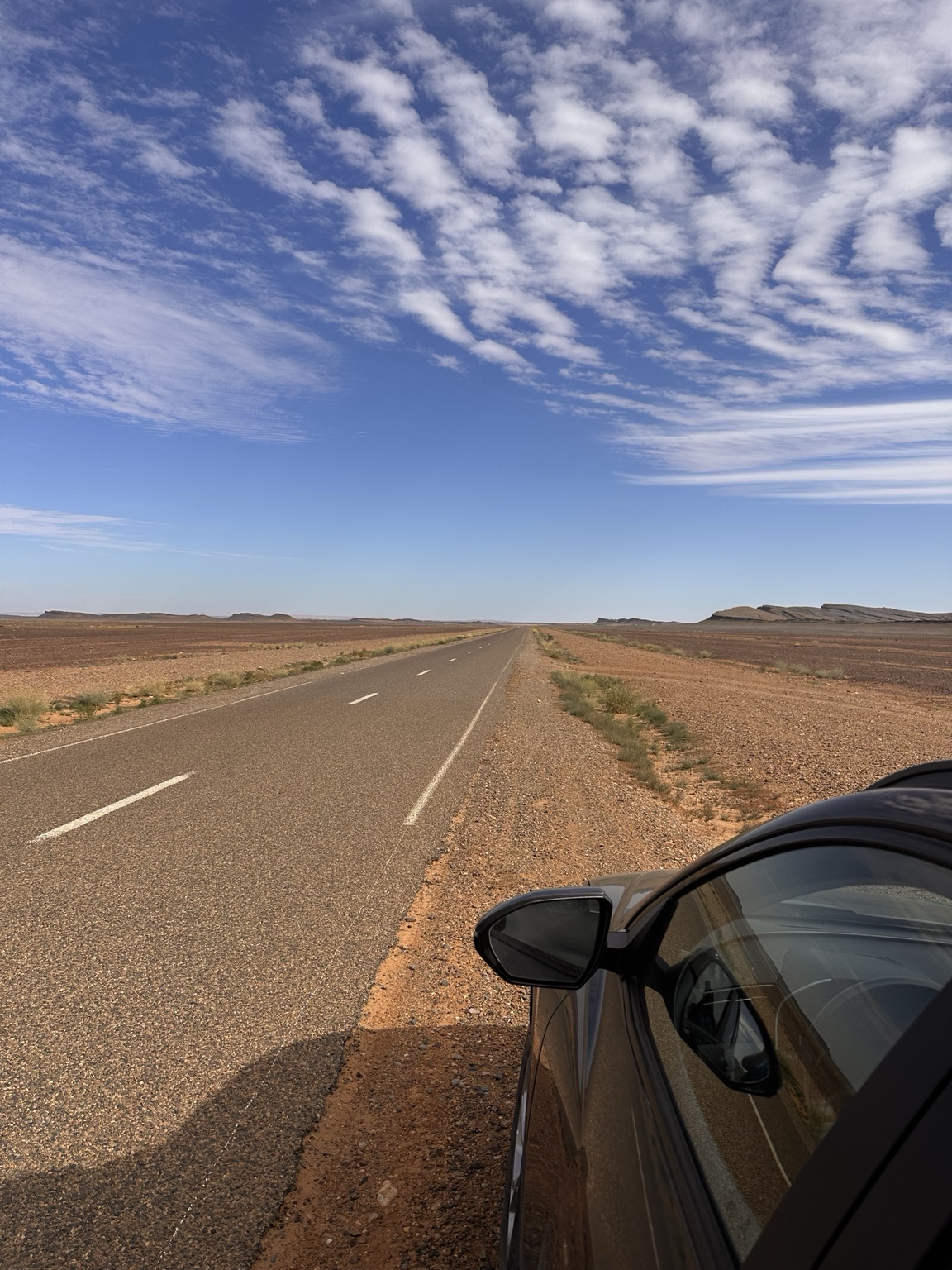 An empty straight road across open country with the parked car at its edge