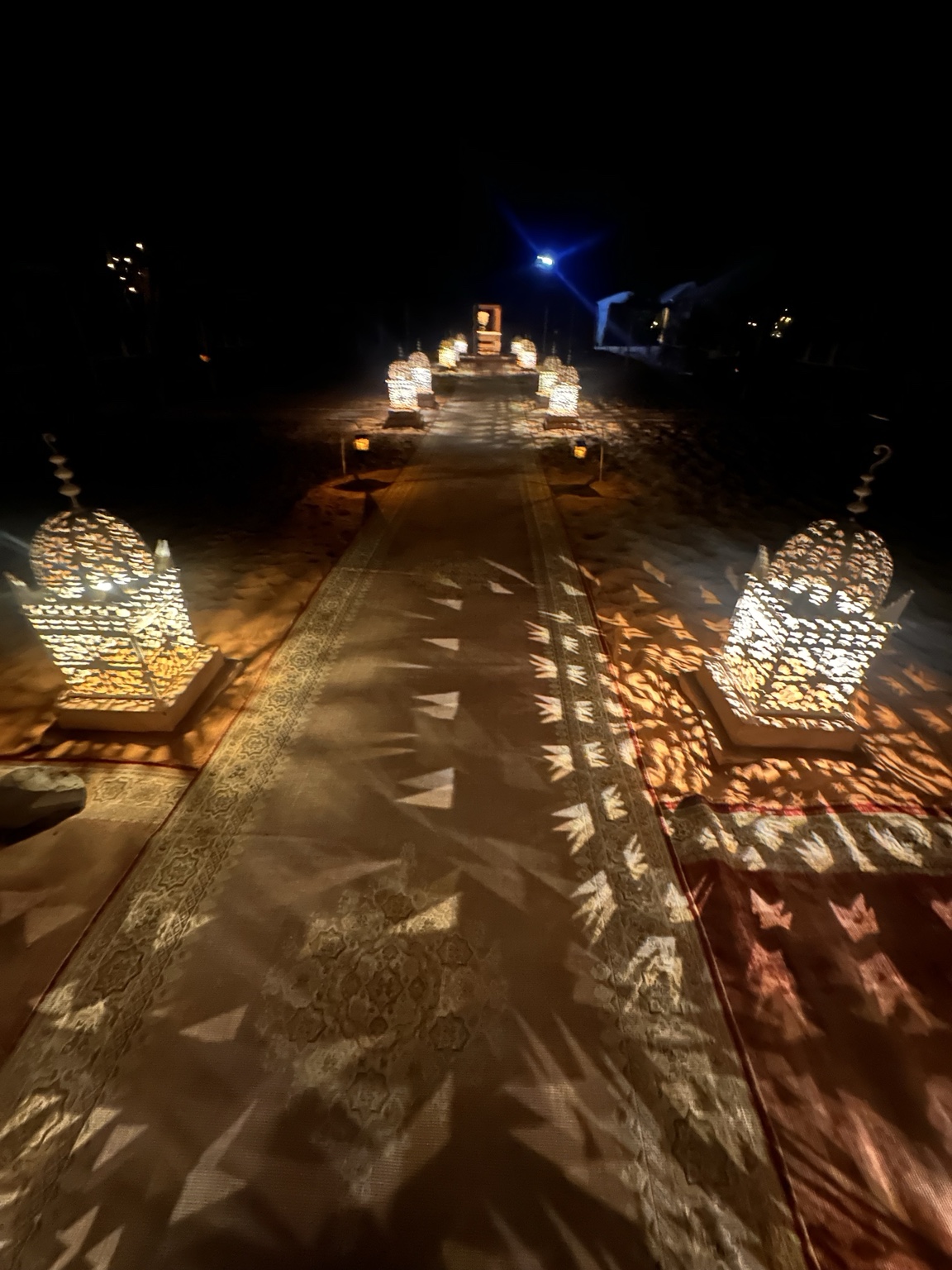 A carpeted path lined with glowing lanterns at the desert camp