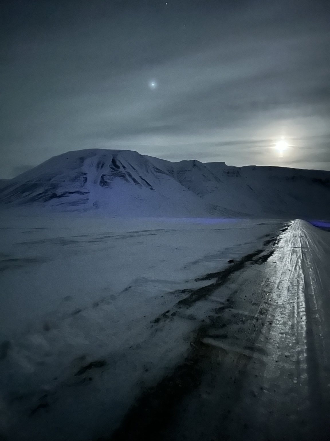 Snowy road stretching toward a mountain under the moon